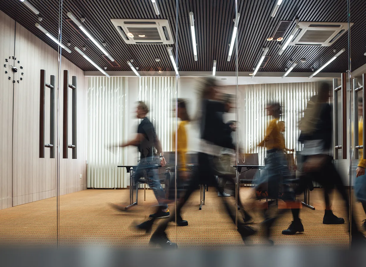 Menschen gehen verschwommen durch einen Flur mit Glastüren.