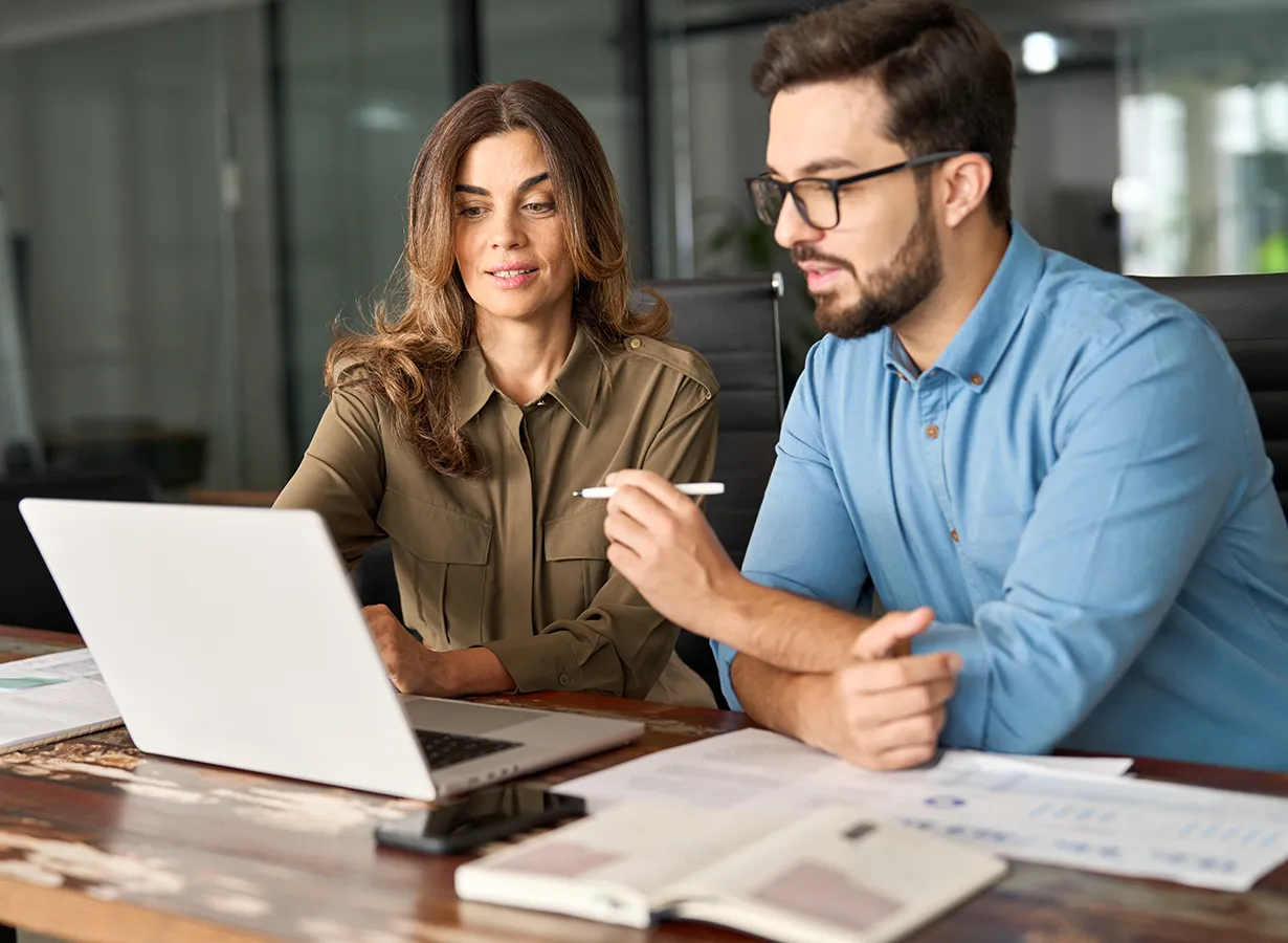 Beratung zur Arbeitsvermittlung: Mann und Frau besprechen Unterlagen am Laptop in einem modernen Büro.