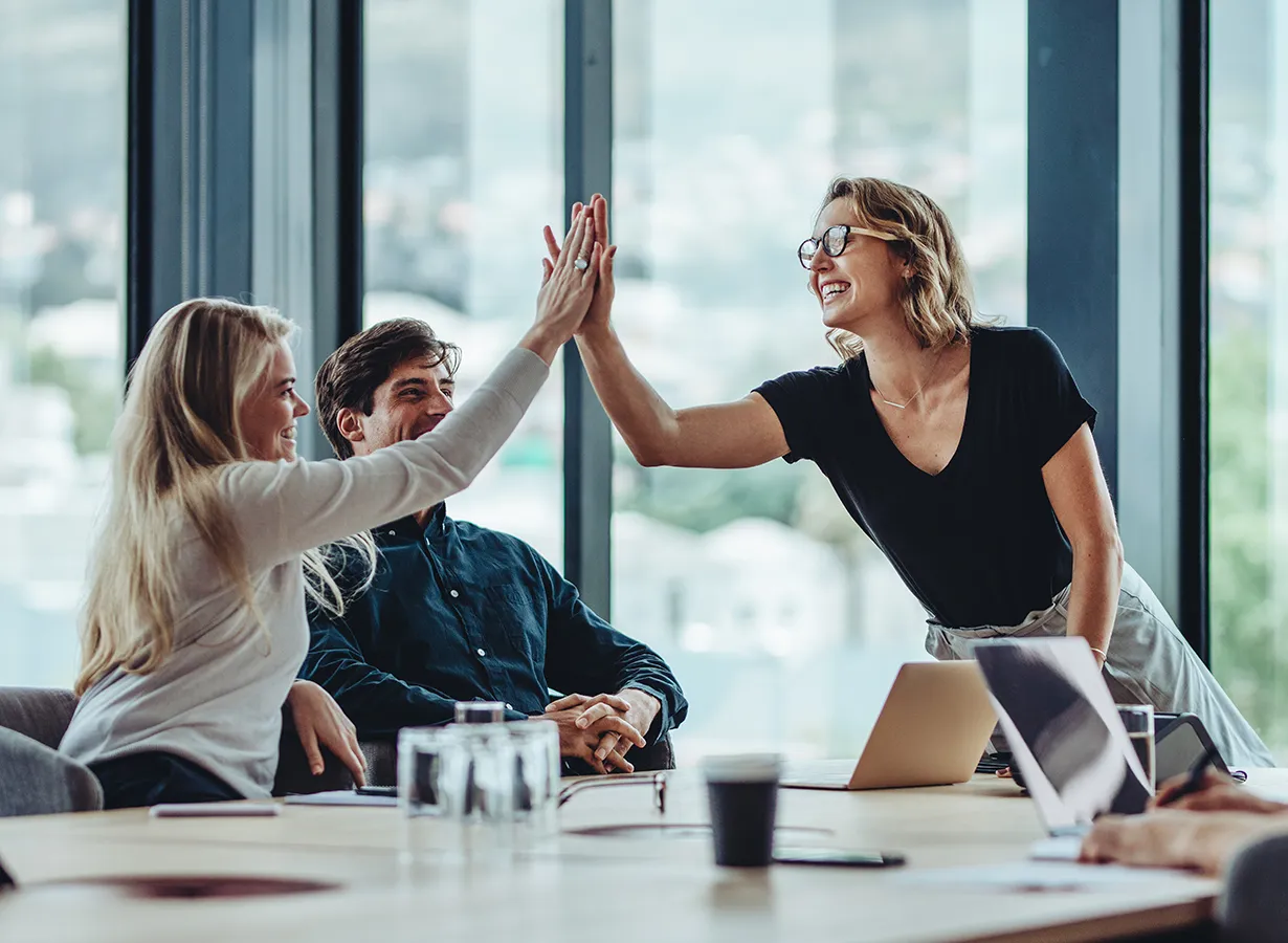 Jobcenter Landsberg am Lech: Teammeeting , zwei Kolleginnen geben sich ein High-Five, ein Kollege lacht im Hintergrund.